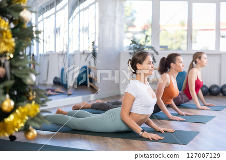 Girl teacher conduct yoga lesson for girls and performs cobra pose in New Year atmosphere Girl teacher conduct yoga lesson for girls and performs cobra pose in New Year atmosphere 127007129
