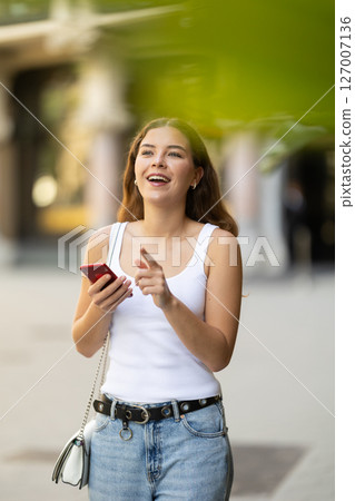 Young smiling girl with phone walks along city street Young smiling girl with phone walks along city street 127007136