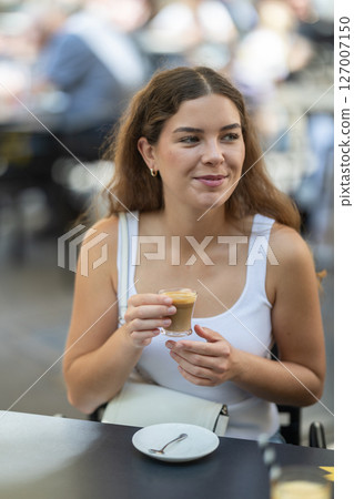 Girl relaxes in street cafe, drinks coffee Girl relaxes in street cafe, drinks coffee 127007150