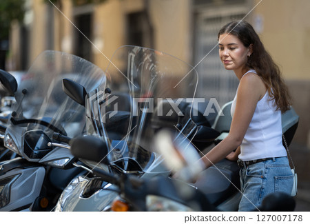Young woman parking scooter in city street on summer day Young woman parking scooter in city street on summer day 127007178