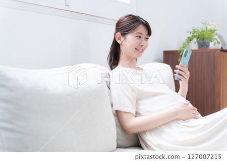 Smiling pregnant woman using a smartphone 127007215