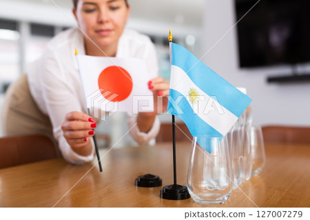 Preparing for business presentation - secretary places flags of Argentina and Japan on negotiating table 127007279