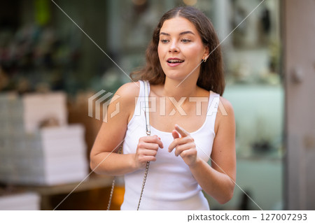 Smiling brunette looking at storefront during city walk 127007293
