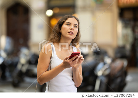 Young girl with mobile phone in her hands walking around the city and taking pictures of sights Young girl with mobile phone in her hands walking around the city and taking pictures of sights 127007294
