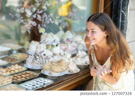 Young tourist girl near window of street cafe food court chooses stuffed puff and cookie Young tourist girl near window of street cafe food court chooses stuffed puff and cookie 127007326