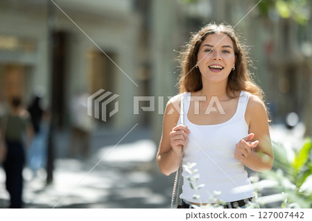 Cheerful girl walking at the street among architecture with bag 127007442