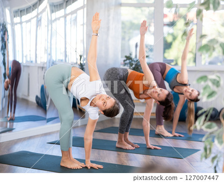 Girl teacher lead lesson, run training in female yoga studio and perform Uttanasana. Girl teacher lead lesson, run training in female yoga studio and perform Uttanasana. 127007447