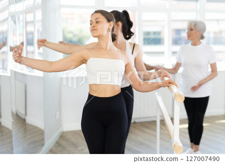 Teacher conducts class with girls in ballet studio, observes doing third position exercise. Teacher conducts class with girls in ballet studio, observes doing third position exercise. 127007490
