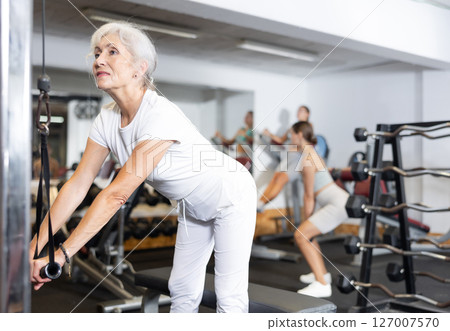 Active athlete mature woman during exercises on crossover exercise machine with loops and weighting 127007570