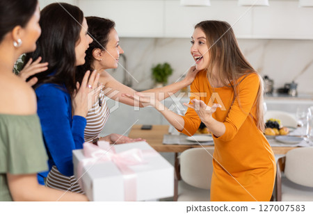 Three women have arrived for birthday celebration and presenting gift to birthday woman 127007583