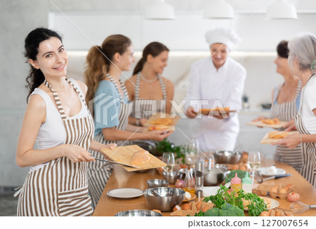 Girl at group class of culinary school cuts up chicken and prepares low-calorie diet lunch 127007654