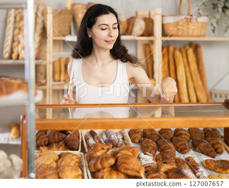 Young woman near window of bakery food court store examines assortment 127007657