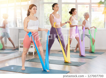 Women are doing stretching exercise with resistance bands in gym. Teamwork, good mood and healthy lifestyle concept Women are doing stretching exercise with resistance bands in gym. Teamwork, good mood and healthy lifestyle concept 127007700