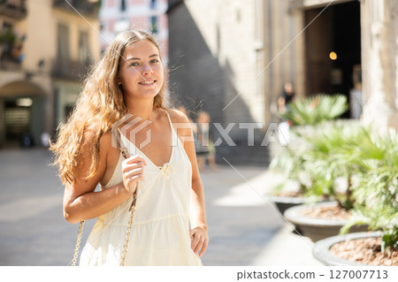 Portrait of a young girl in a light summer dress on city street during the day Portrait of a young girl in a light summer dress on city street during the day 127007713