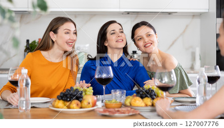 Girlfriends drinking wine and having conversation over dinner at house party Girlfriends drinking wine and having conversation over dinner at house party 127007776