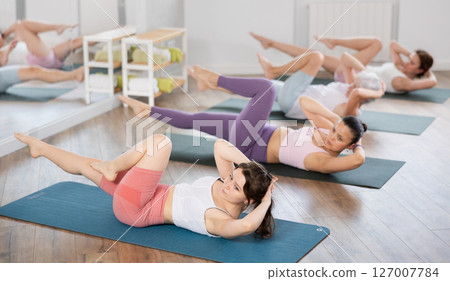 Girl doing bicycle crunches during group pilates training Girl doing bicycle crunches during group pilates training 127007784