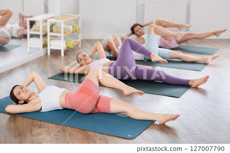Young girl doing Supta Matsyendrasana during group yoga practice Young girl doing Supta Matsyendrasana during group yoga practice 127007790