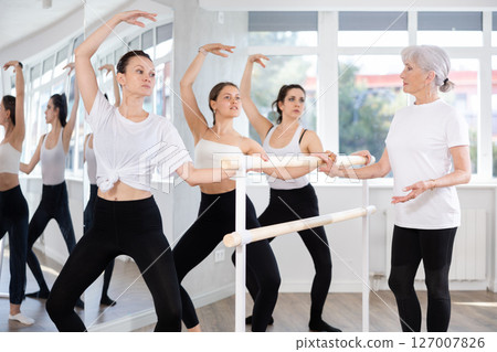 Woman practicing demi plie at barre during group ballet class Woman practicing demi plie at barre during group ballet class 127007826