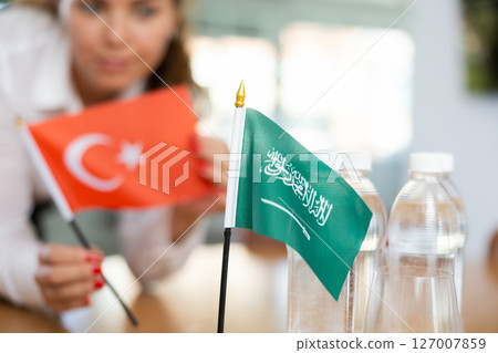 Woman secretary prepares an office for negotiations - she places flags of Saudi Arabia and Turkish table 127007859