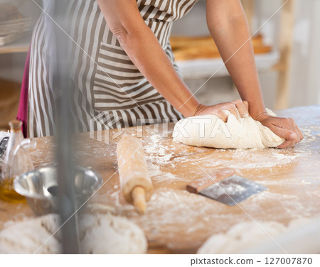 Closeup on pastry chef female hands kneading dough on table at bakery, culinary arts 127007870