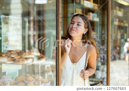 Young tourist girl near window of street cafe food court chooses stuffed puff and cookie Young tourist girl near window of street cafe food court chooses stuffed puff and cookie 127007883