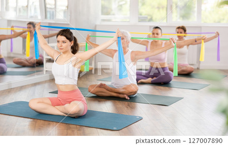 Group Pilates classes - woman doing body stretching using elastic bands in gym 127007890