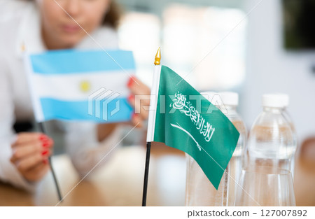 Employee of delegation prepares negotiating table - sets up flag of Saudi Aarabia and Argentine 127007892