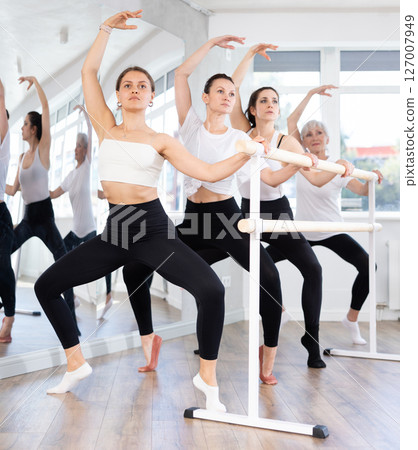 Group of women perform plie at ballet barre 127007949