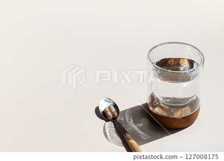Two Pills on Spoon and Glass of Water are Ready for Daily Vitamins Intake Promoting Health and Wellness. 127008175