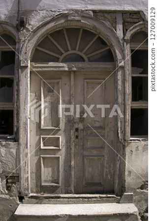 Old wooden door on a house wall. Conceptual image. Wooden Door on an Old House Wall. Architectural Details Worn and Weathered by Time. Old wooden door on a house wall. Conceptual image. Wooden Door on an Old House Wall. Architectural Details Worn and Weathered by Time. 127009129