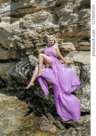 Woman Dress Rocks: Woman poses in purple dress on rocks in daylight for photoshoot, stylish. 127009165