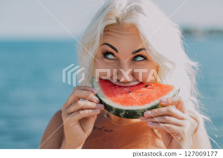 Watermelon Woman Summer Beach: Happy blonde enjoys juicy watermelon slice near ocean during sunny day. Watermelon Woman Summer Beach: Happy blonde enjoys juicy watermelon slice near ocean during sunny day. 127009177