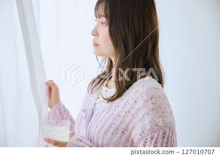 A woman drinking a glass of juice by the window 127010707