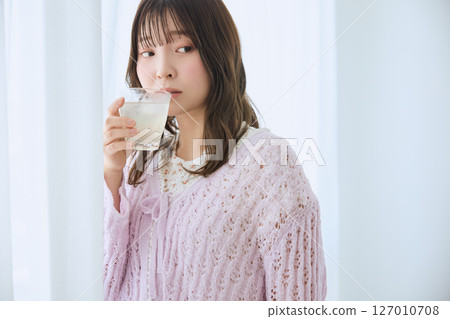 A woman drinking a glass of juice by the window 127010708