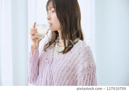 A woman drinking a glass of juice by the window 127010709
