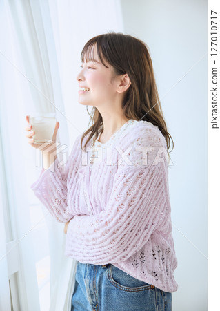 A woman drinking a glass of juice by the window A woman drinking a glass of juice by the window 127010717