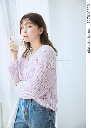 A woman drinking a glass of juice by the window 127010720