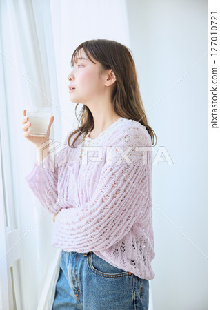 A woman drinking a glass of juice by the window 127010721