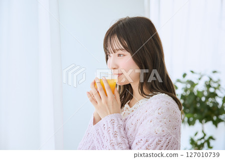 A woman drinking a glass of juice by the window 127010739