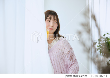 A woman drinking a glass of juice by the window A woman drinking a glass of juice by the window 127010751