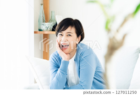 Middle-aged woman sitting on sofa in living room 127011250