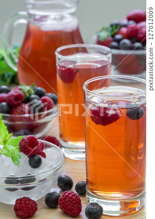 2 compotes of raspberries, strawberries, blueberries, near bowl of ice, 2 bowls of berries, mint leaves, carafe compote, straws on light background scattered berries. Berries compote. Vertical. Close. 2 compotes of raspberries, strawberries, blueberries, near bowl of ice, 2 bowls of berries, mint leaves, carafe compote, straws on light background scattered berries. Berries compote. Vertical. Close. 127012009