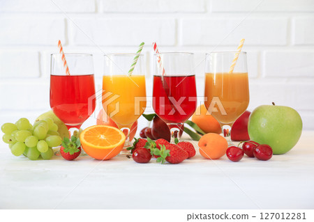 Freshly prepared fruit juices showcase bright colors in transparent glasses with colorful straws set against a clean white backdrop. Juicy fruits surround each glass on white background. 127012281