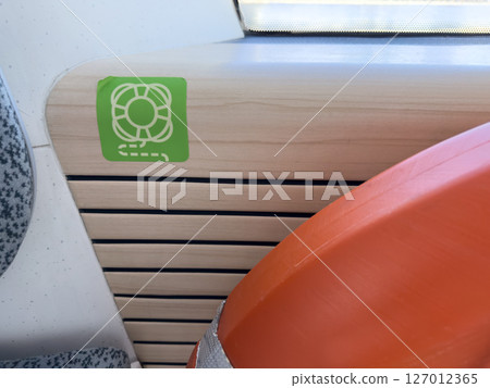 Emergency life ring symbol on wooden interior panel of a modern passenger vessel. Maritime safety signage indicating the location of life saving equipment onboard public water transport 127012365