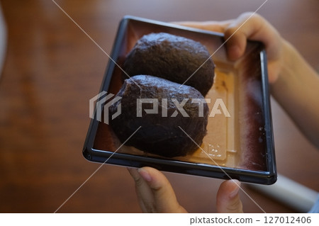 Handmade ohagi rice balls in a Japanese-style paper container and a child's hand holding it 127012406