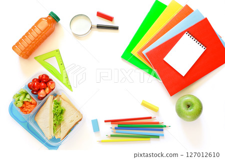School supplies, lunch box with sandwiches, pieces of cucumbers and carrots, cherries, apple, bottle of juice on white background, back to school concept with copyspace. Horizontal. Top view. 127012610