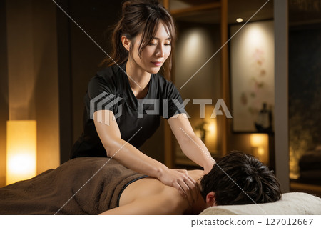A young female staff member at a men's beauty salon relieves a man's stiff shoulders 127012667