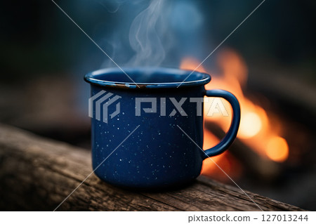 Blue Enamel Mug of Hot Coffee on Wooden Log Near Outdoor Campfire 127013244