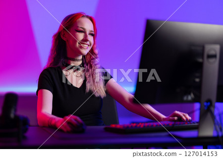 Smiling gamer enthusiast working at a computer in a colorful gaming setup 127014153