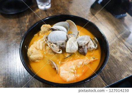 close up of laksa rice noodles with seafood including shells, prawn, clam, tofu puff in a black bowl 127014230